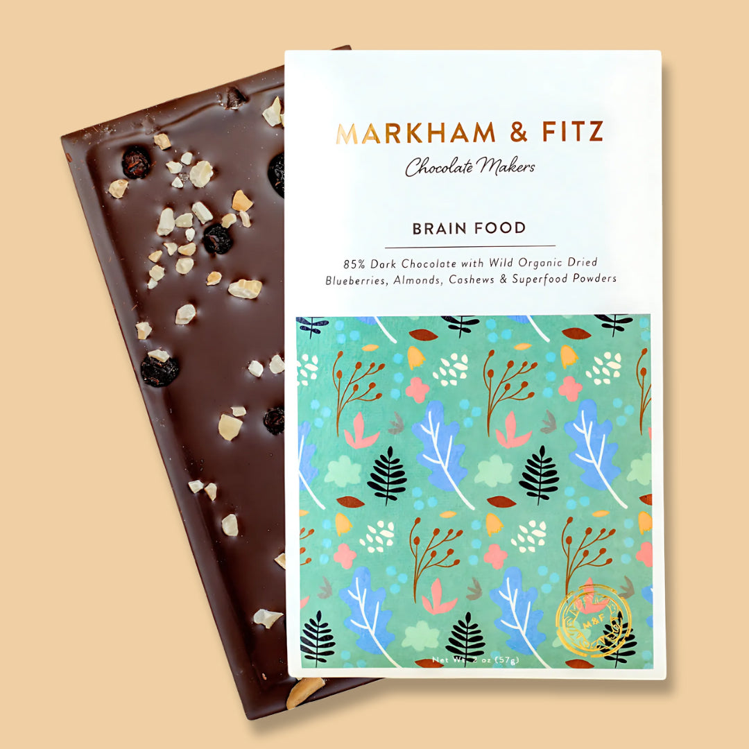 Markham &amp; Fitz Brain Food bar beside its white and teal botanical sleeve, dark chocolate topped with blueberries and chopped nuts