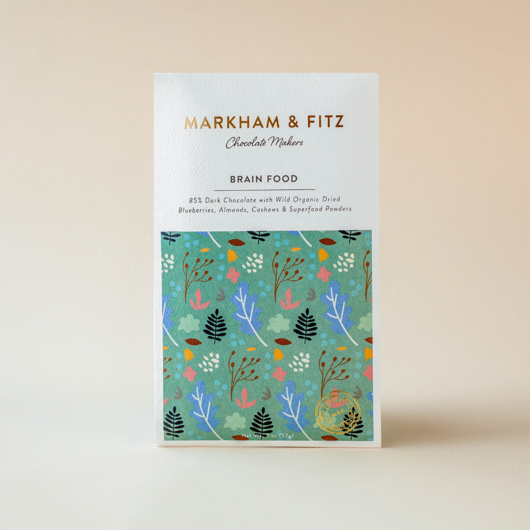 Brain Food dark chocolate bar in its white sleeve with a teal botanical illustration, standing upright