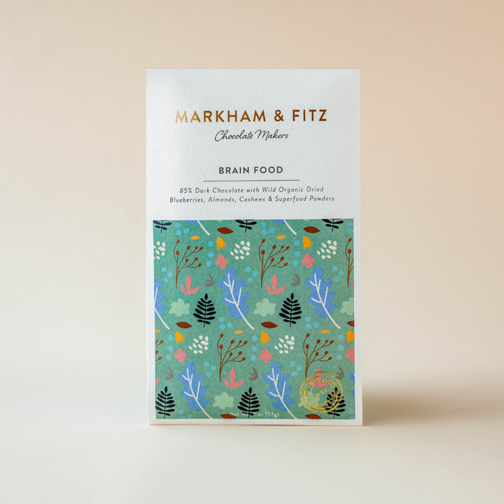Brain Food dark chocolate bar in its white sleeve with a teal botanical illustration, standing upright