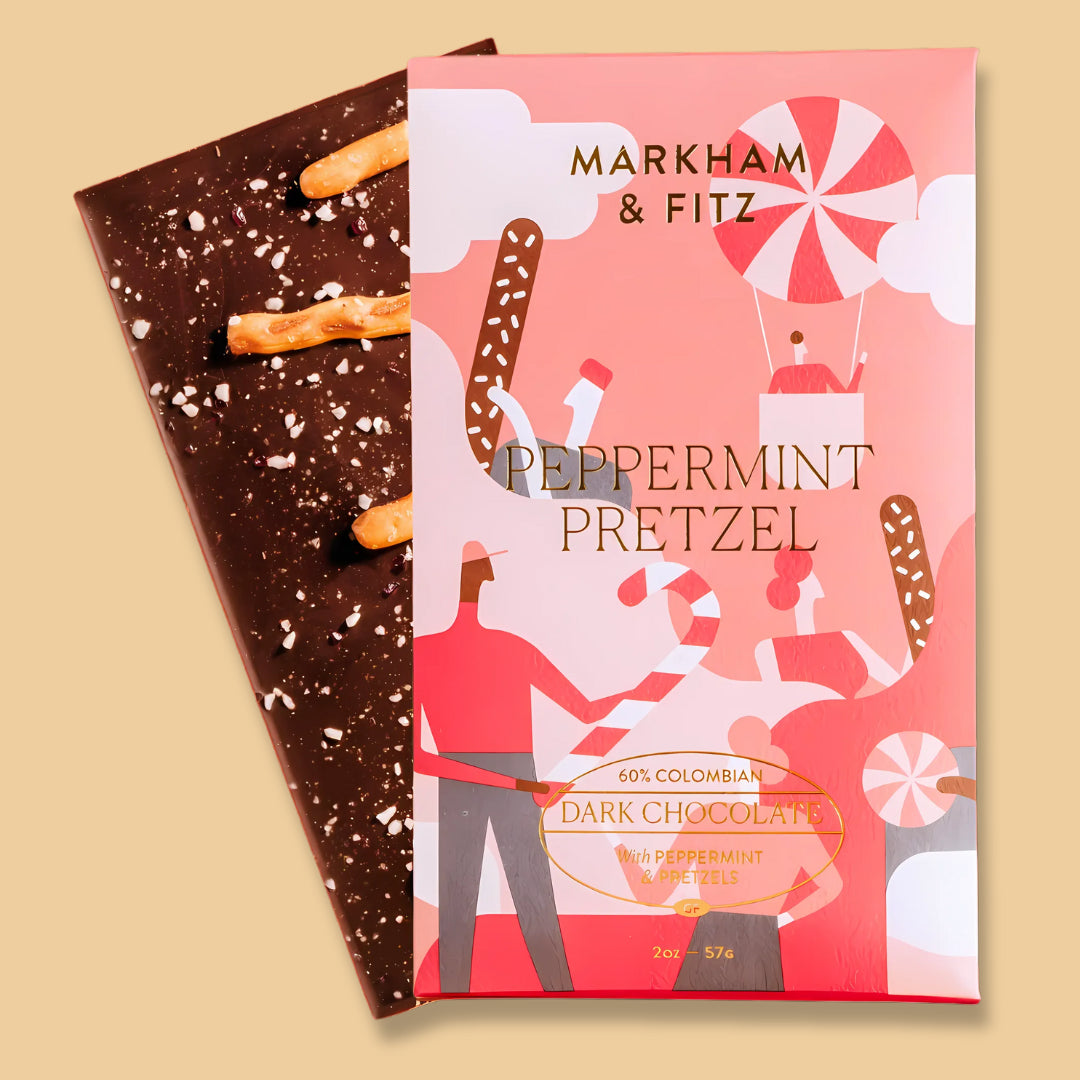 Peppermint Pretzel bar in its coral holiday sleeve, with the dark chocolate bar behind it topped with pretzel pieces and crushed peppermint