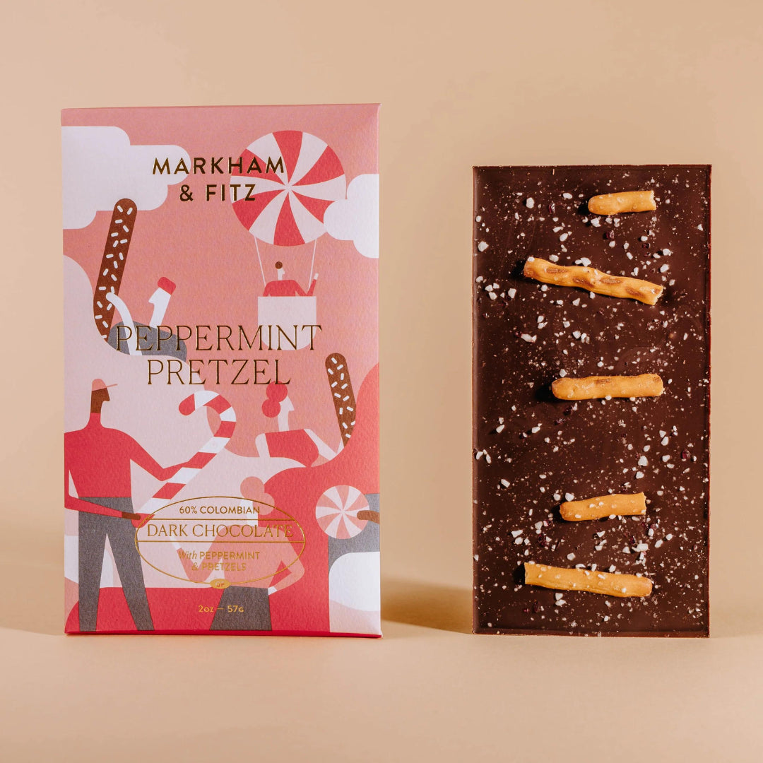 Peppermint Pretzel dark chocolate bar standing next to its illustrated coral and red sleeve