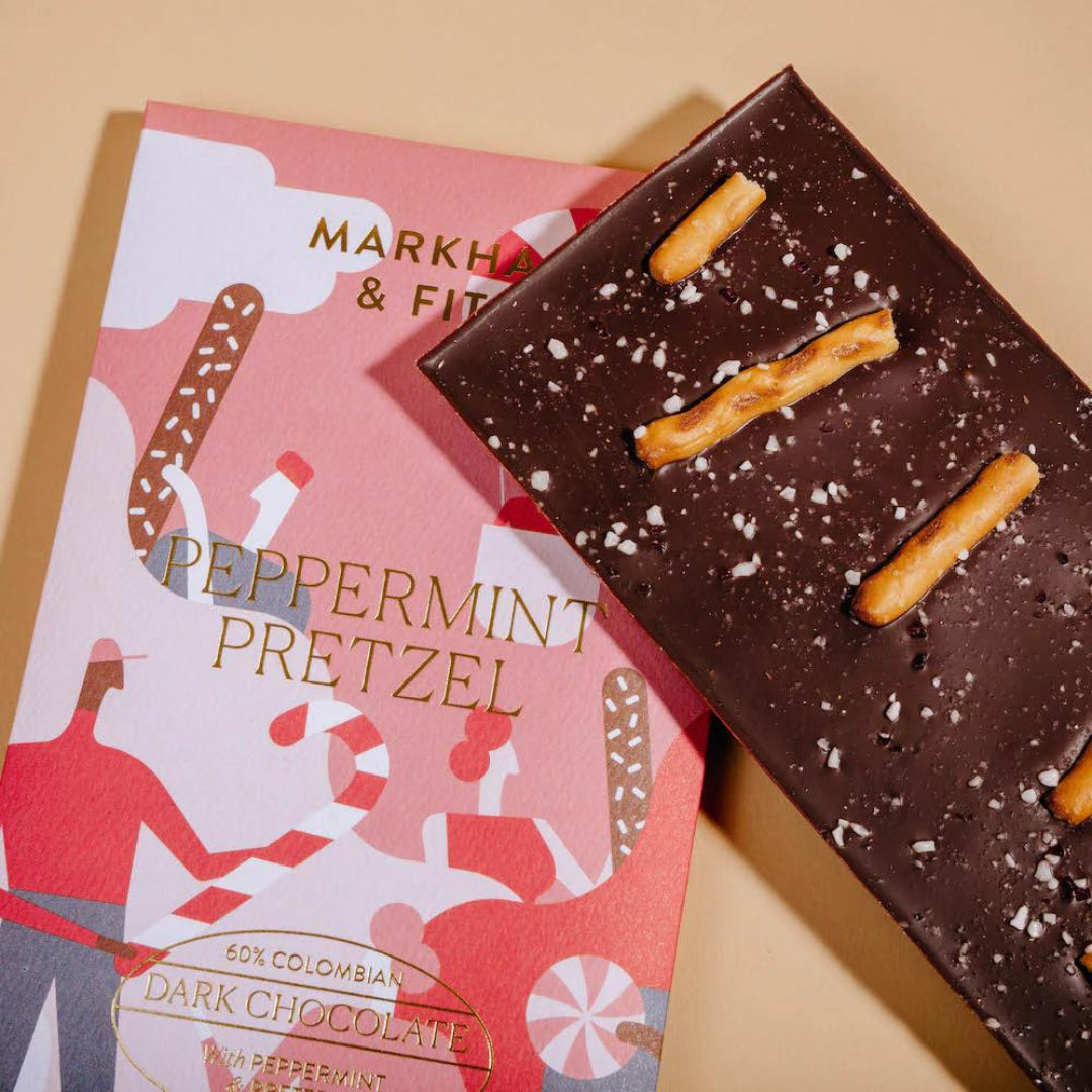 Close view of the Peppermint Pretzel dark chocolate bar with pretzel sticks and crushed peppermint, angled over its sleeve