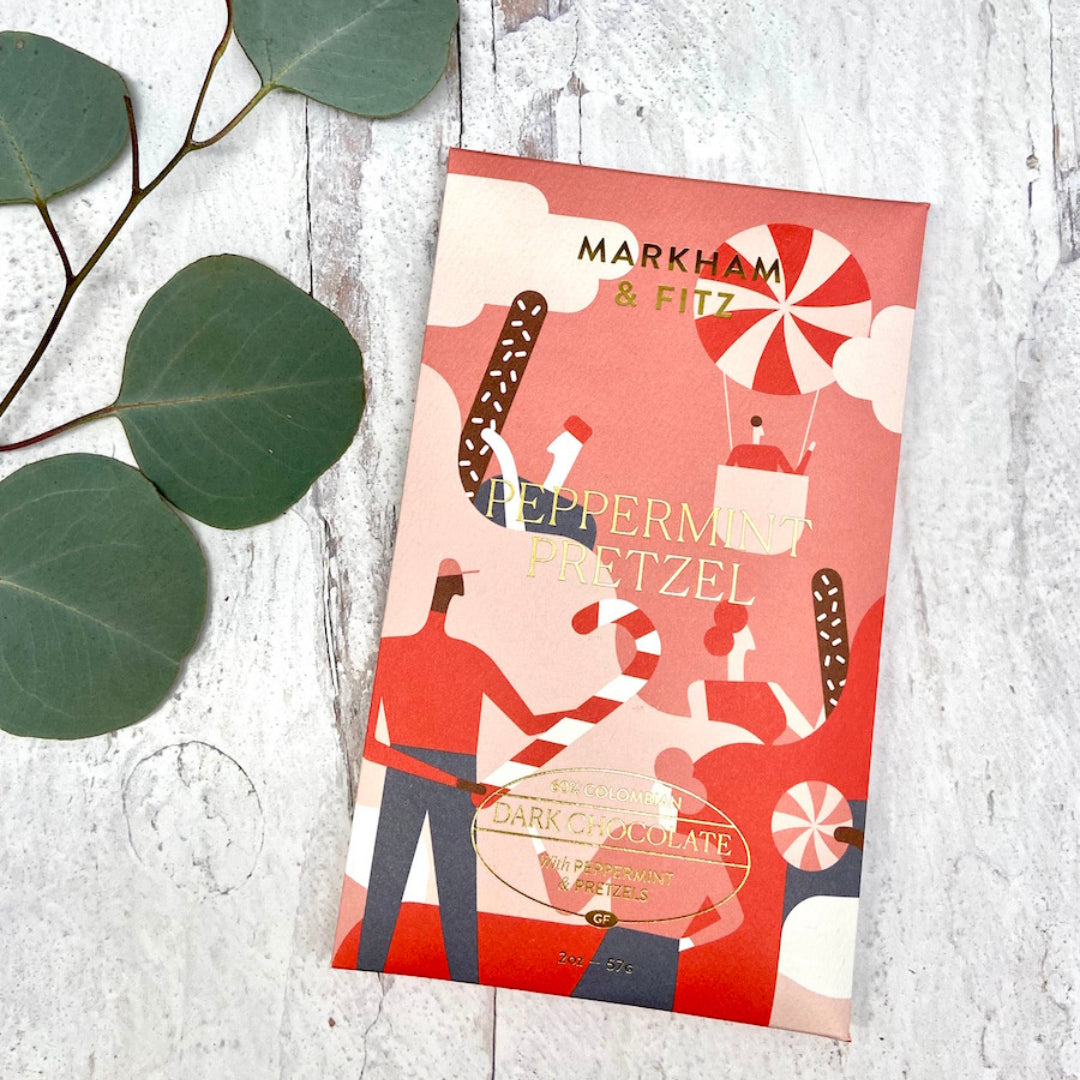 Peppermint Pretzel bar in its illustrated holiday sleeve on a white wood surface with eucalyptus leaves