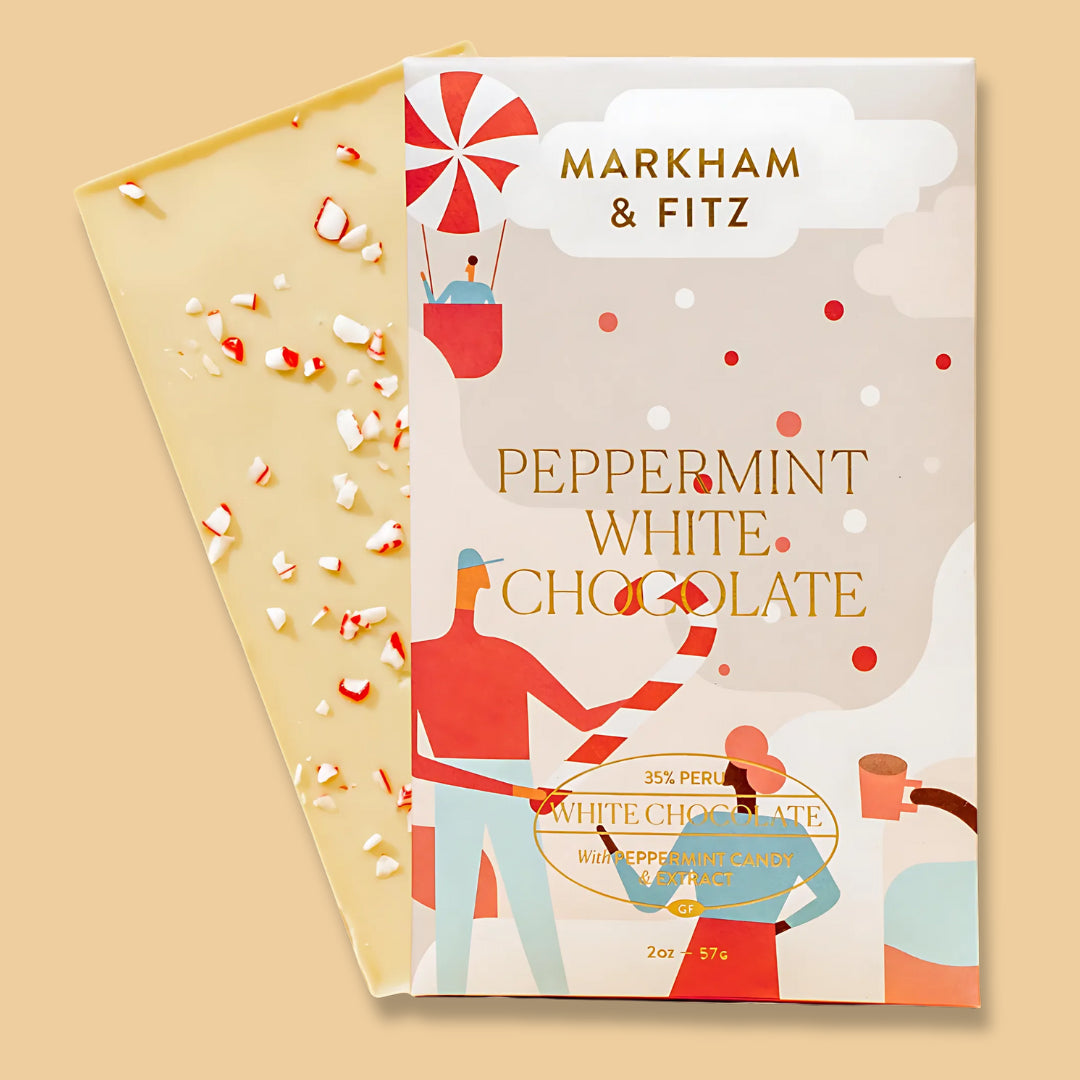 Peppermint White Chocolate bar in its cream holiday sleeve, with the white chocolate bar behind it scattered with red and white peppermint candy