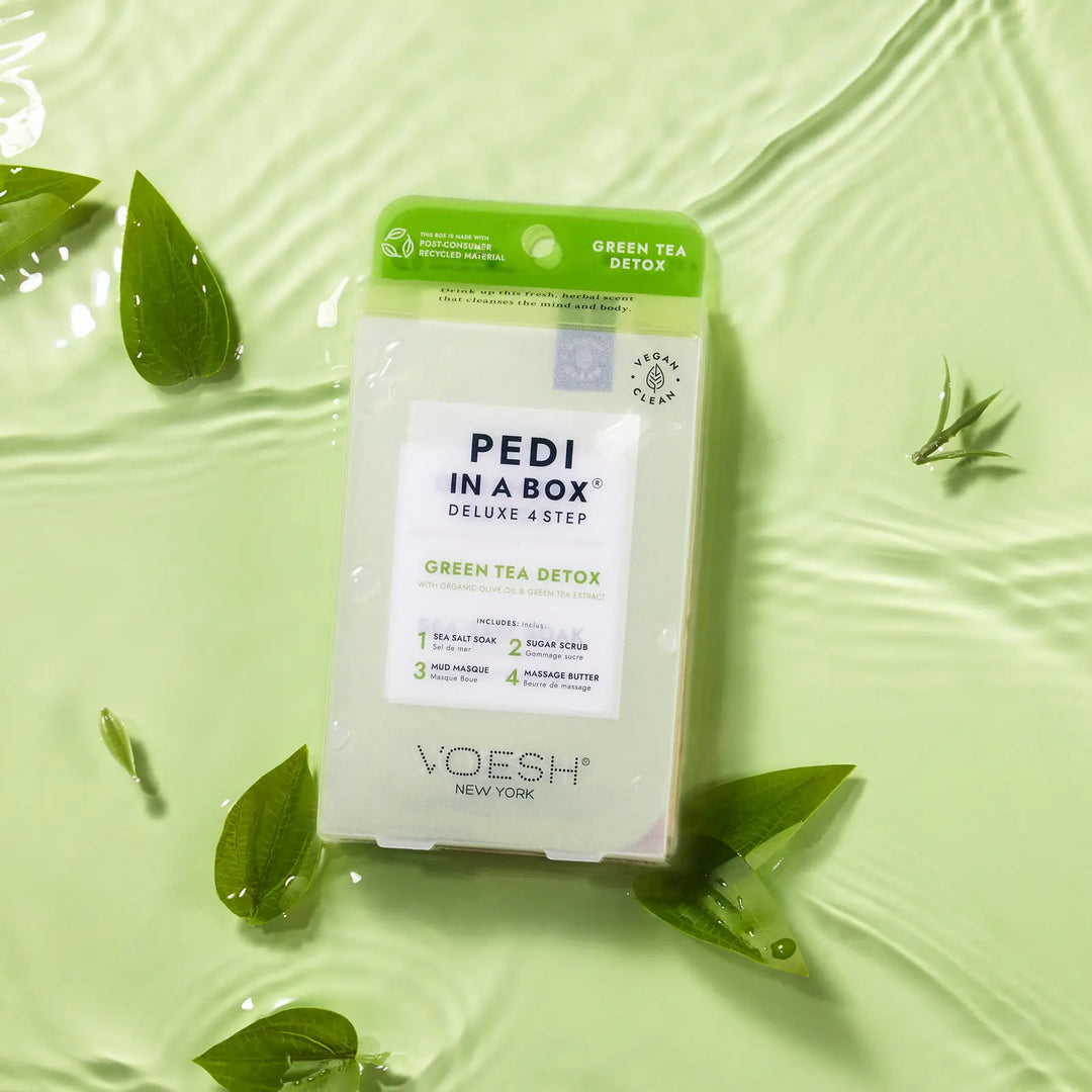 VOESH Pedi in a Box Green Tea Detox Deluxe 4 step kit floating on pale green water with tea leaves