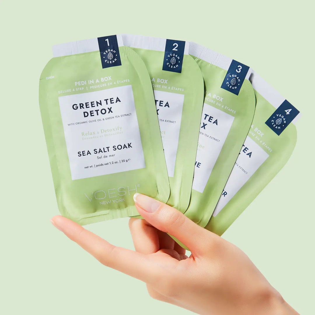 Hand holding the four numbered VOESH Pedi in a Box Green Tea Detox step packets