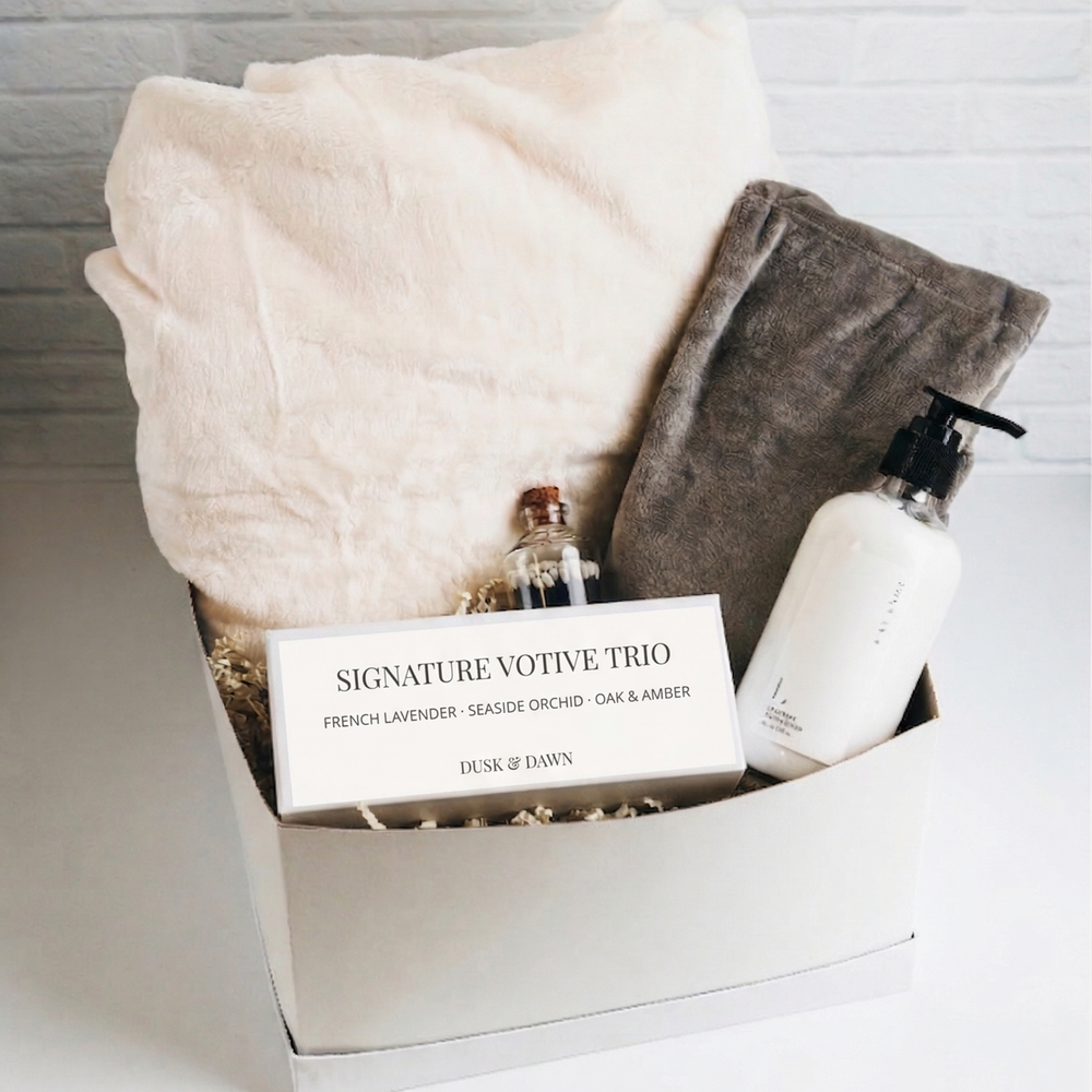 White gift box with plush blanket, scented candles, hand lotion, and matches