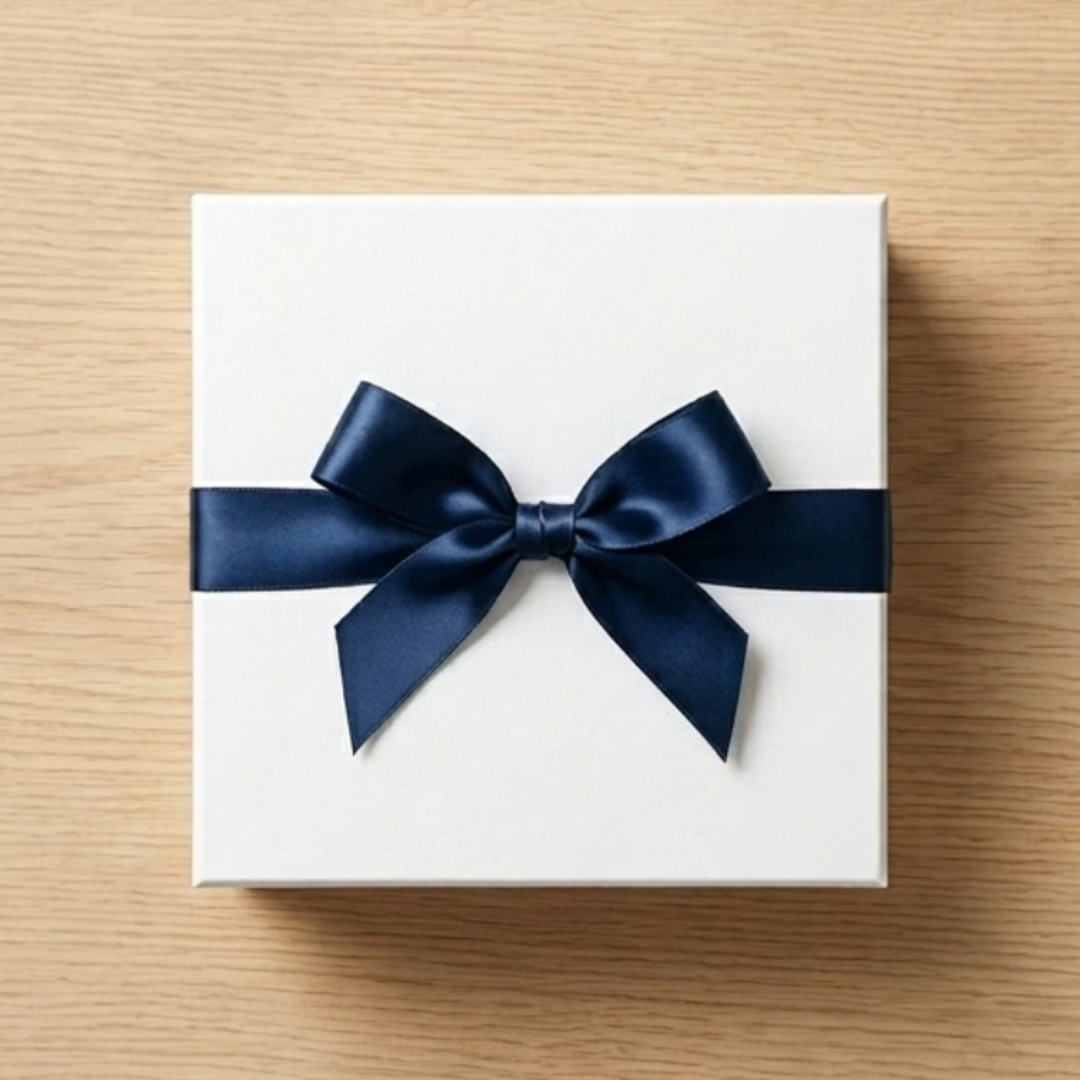 White gift box with navy satin ribbon bow on a light wood surface
