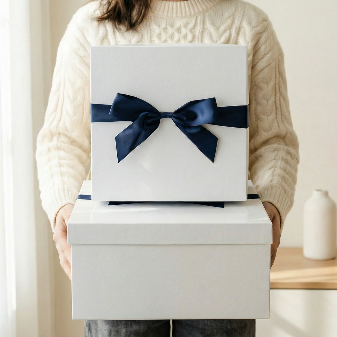 Person holding stacked white gift boxes, top box tied with navy ribbon