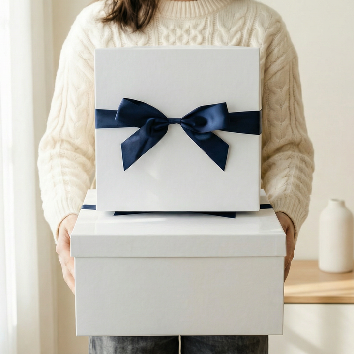 Person holding stacked white gift boxes, top box tied with navy ribbon