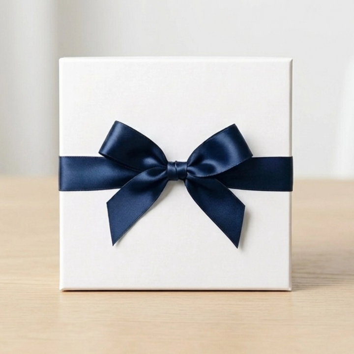White gift box with navy satin ribbon bow on a light wooden surface