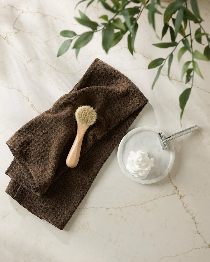 Espresso brown waffle-weave hand towel folded on marble with a wooden face brush and a shaving dish
