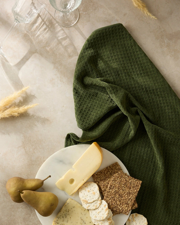 Matcha green waffle-weave hand towel draped on stone beside a marble board with cheese, crackers, and pears