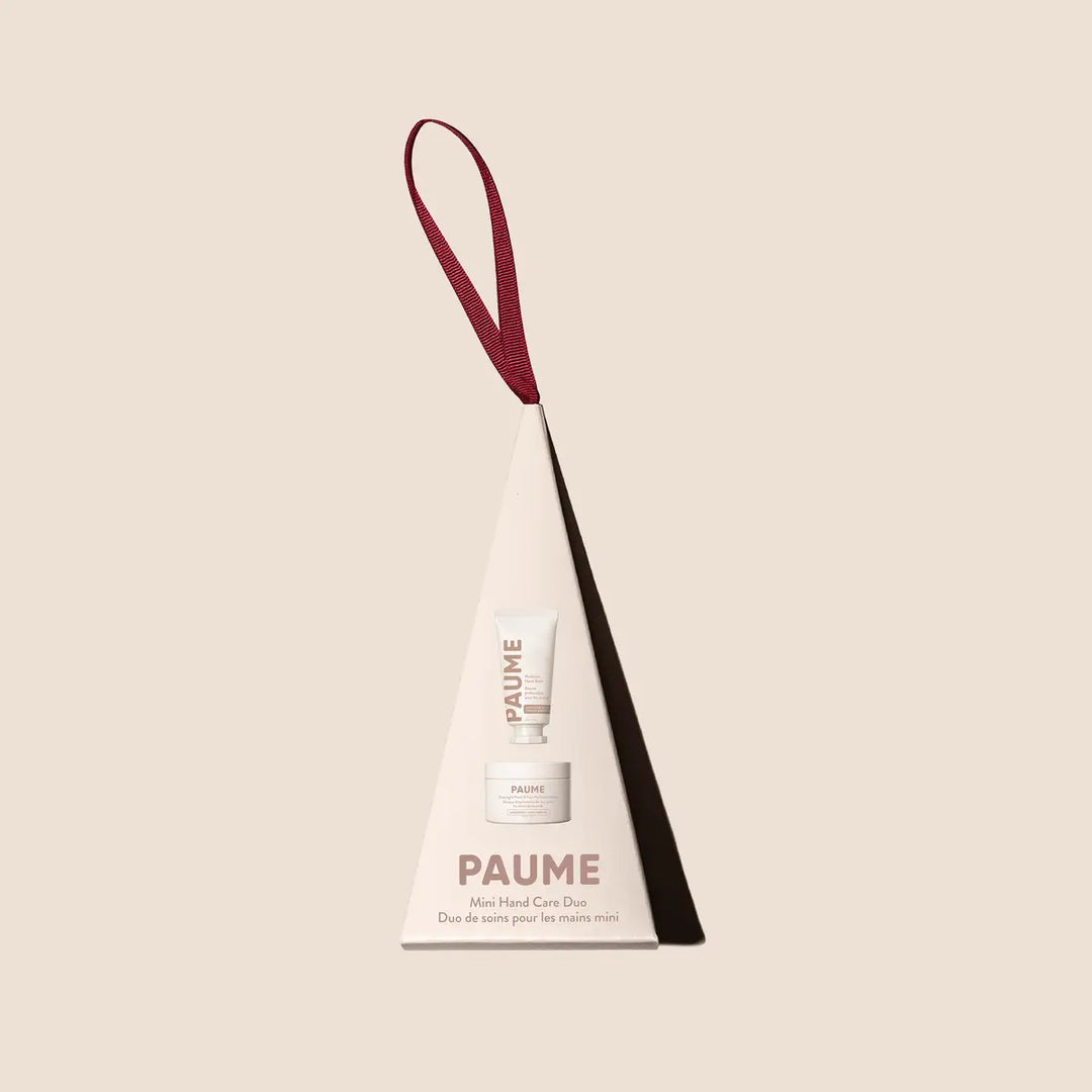 PAUME Mini Hand Care Duo ornament, a cream tree-shaped box with a burgundy ribbon hanger, on a blush background.
