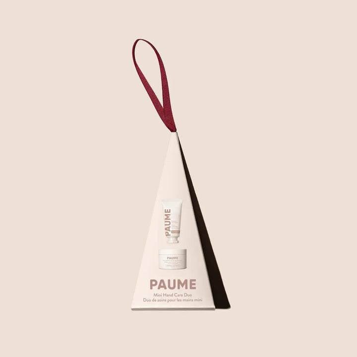 PAUME Mini Hand Care Duo ornament, a cream tree-shaped box with a burgundy ribbon hanger, on a blush background.