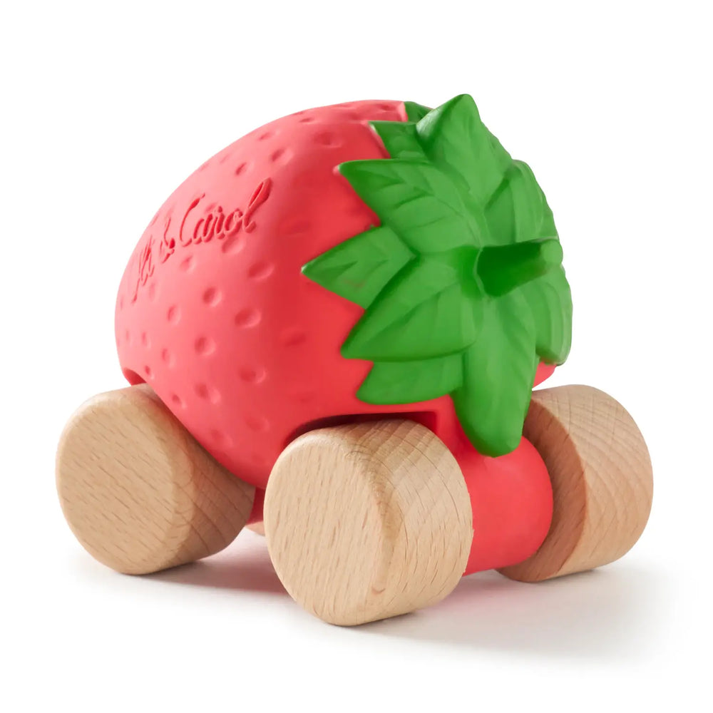 Three-quarter rear view of the red rubber strawberry car, showing the green leaves and the wooden wheels.
