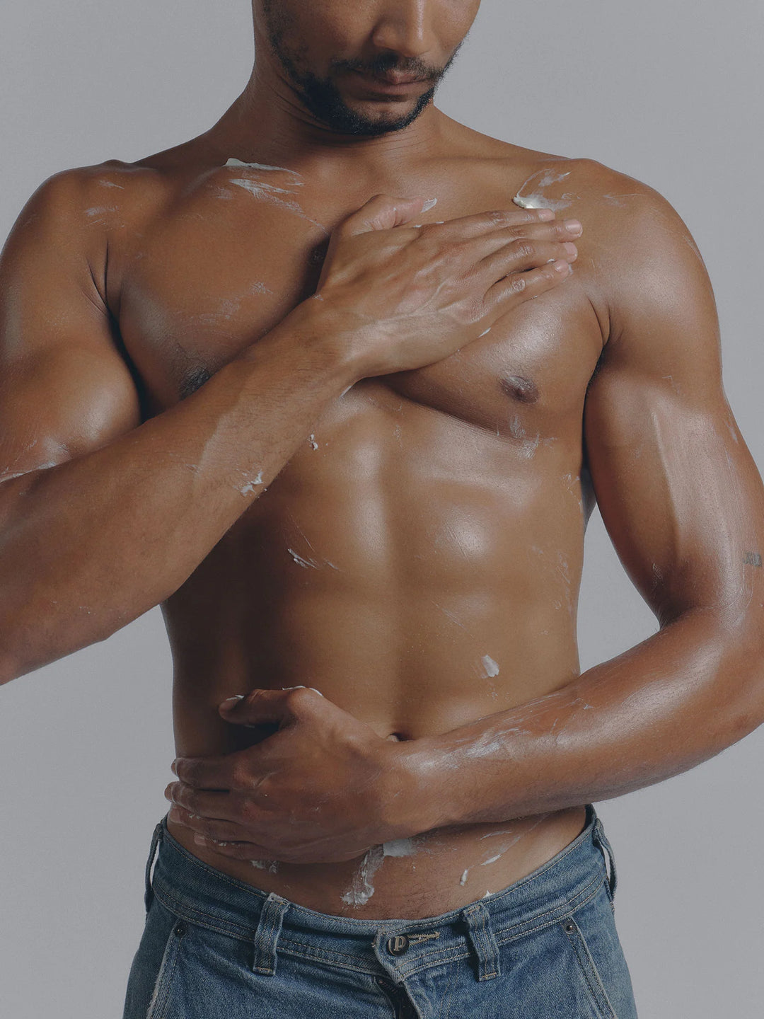 Person with white cream smoothed across the chest and torso, standing against a grey background