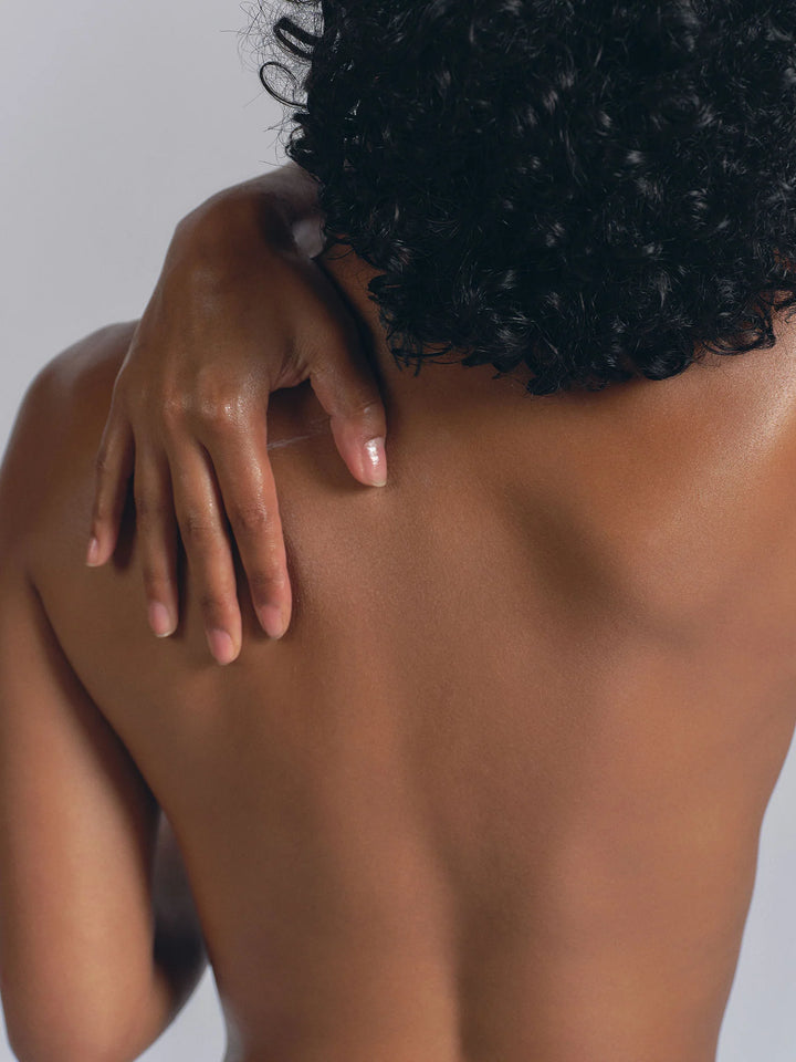 View of a bare back with a hand resting on the shoulder, skin lightly moisturized