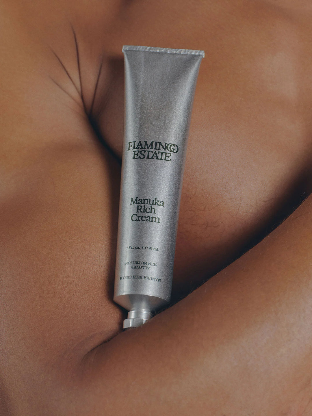 Silver aluminum cream tube lying on bare skin, the Flamingo Estate label and 2.5 fl oz marking visible