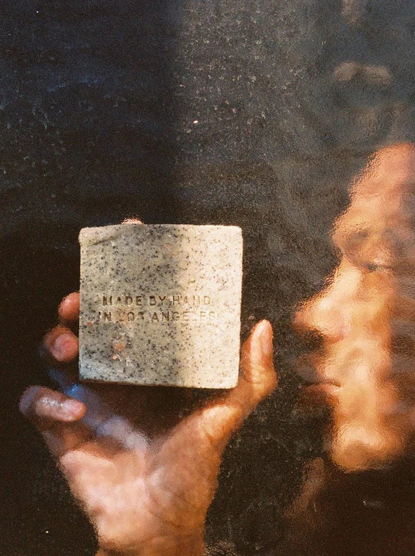 A hand holding the soap brick against steamy glass, the reverse face embossed Made by Hand in Los Angeles