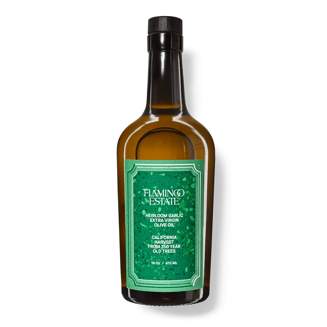 Flamingo Estate Heirloom Garlic Extra Virgin Olive Oil in an amber glass bottle with a green label and black cap, upright on a white background