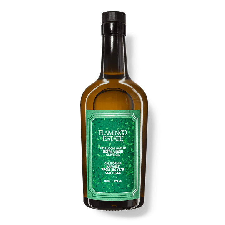 Flamingo Estate Heirloom Garlic Extra Virgin Olive Oil in an amber glass bottle with a green label and black cap, upright on a white background