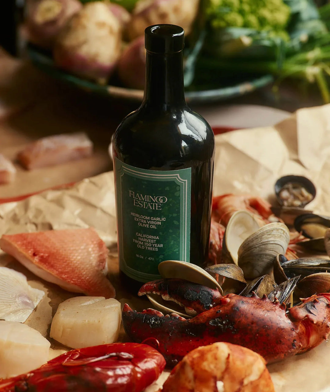 The green-labeled olive oil bottle standing on butcher paper among raw scallops, clams, shrimp and a lobster claw