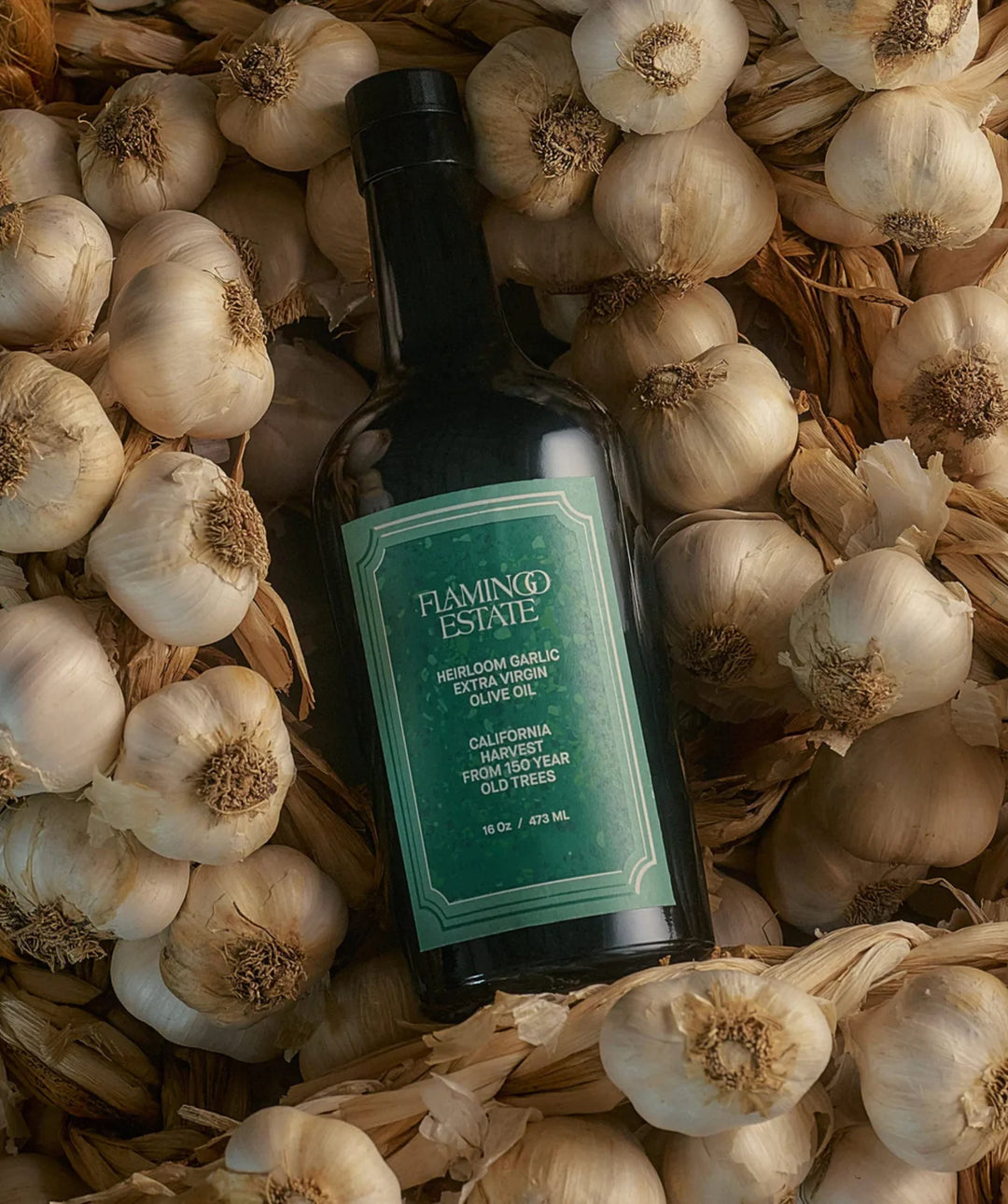 The dark bottle lying flat on a bed of whole garlic bulbs, green label facing up