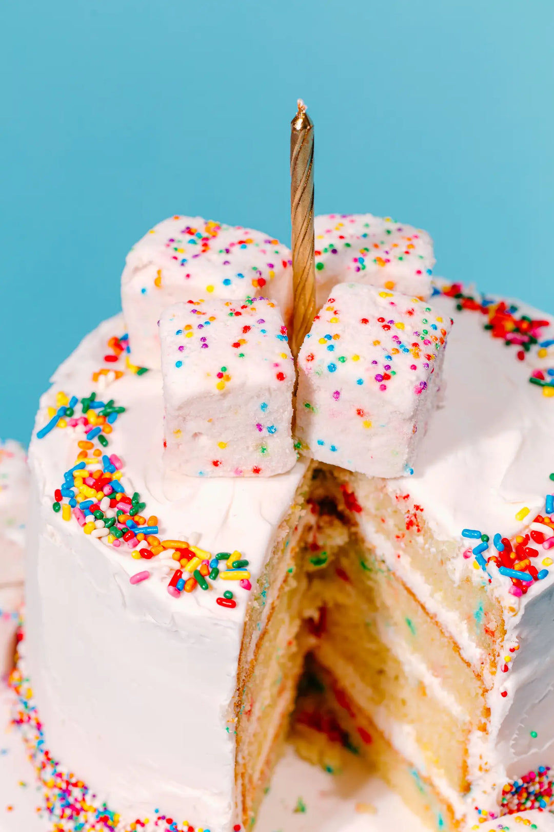 Sprinkle cake topped with stacked marshmallows around a gold birthday candle