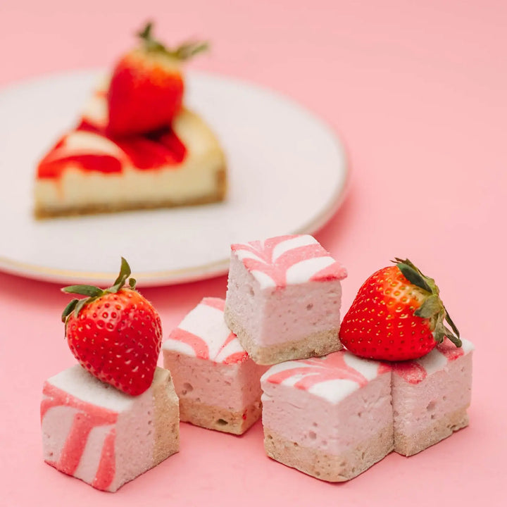 Strawberry swirl marshmallows with fresh strawberries in front of a plate holding a slice of strawberry cheesecake