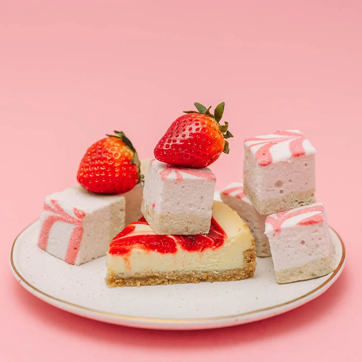 Plate of strawberry cheesecake topped with pink swirl marshmallows and whole strawberries