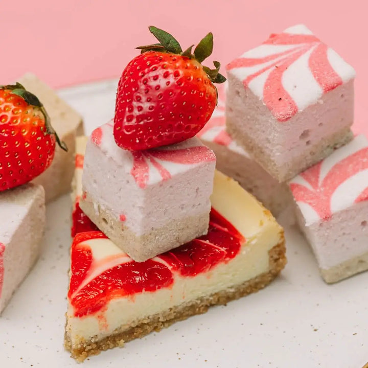 Close view of a pink swirl marshmallow with a strawberry on top, resting on a slice of cheesecake