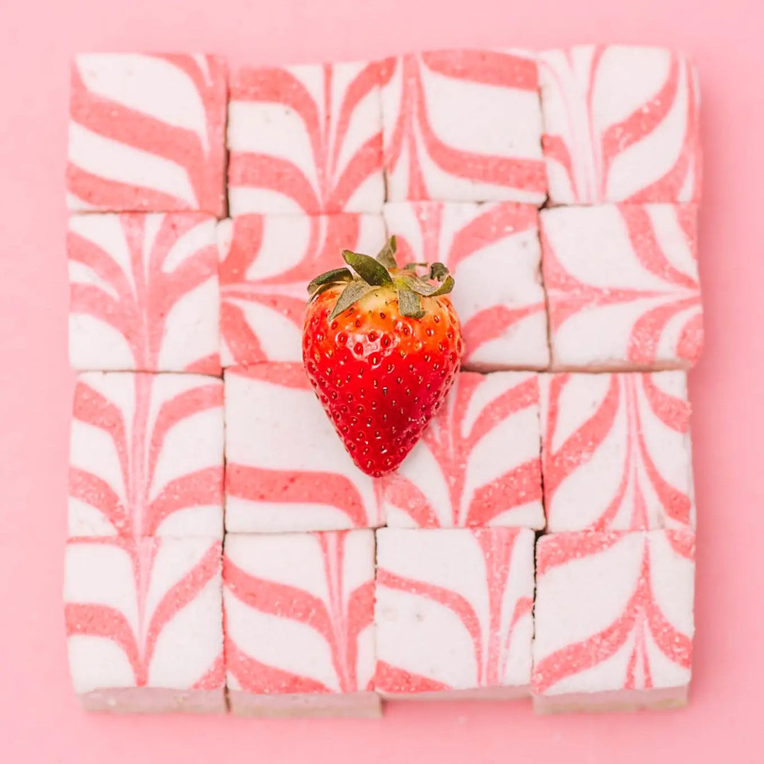 Grid of pink and white swirled marshmallow squares with a strawberry at the center on a pink background
