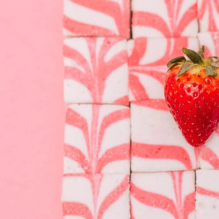 Close crop of swirled strawberry marshmallows with a strawberry on a pink background