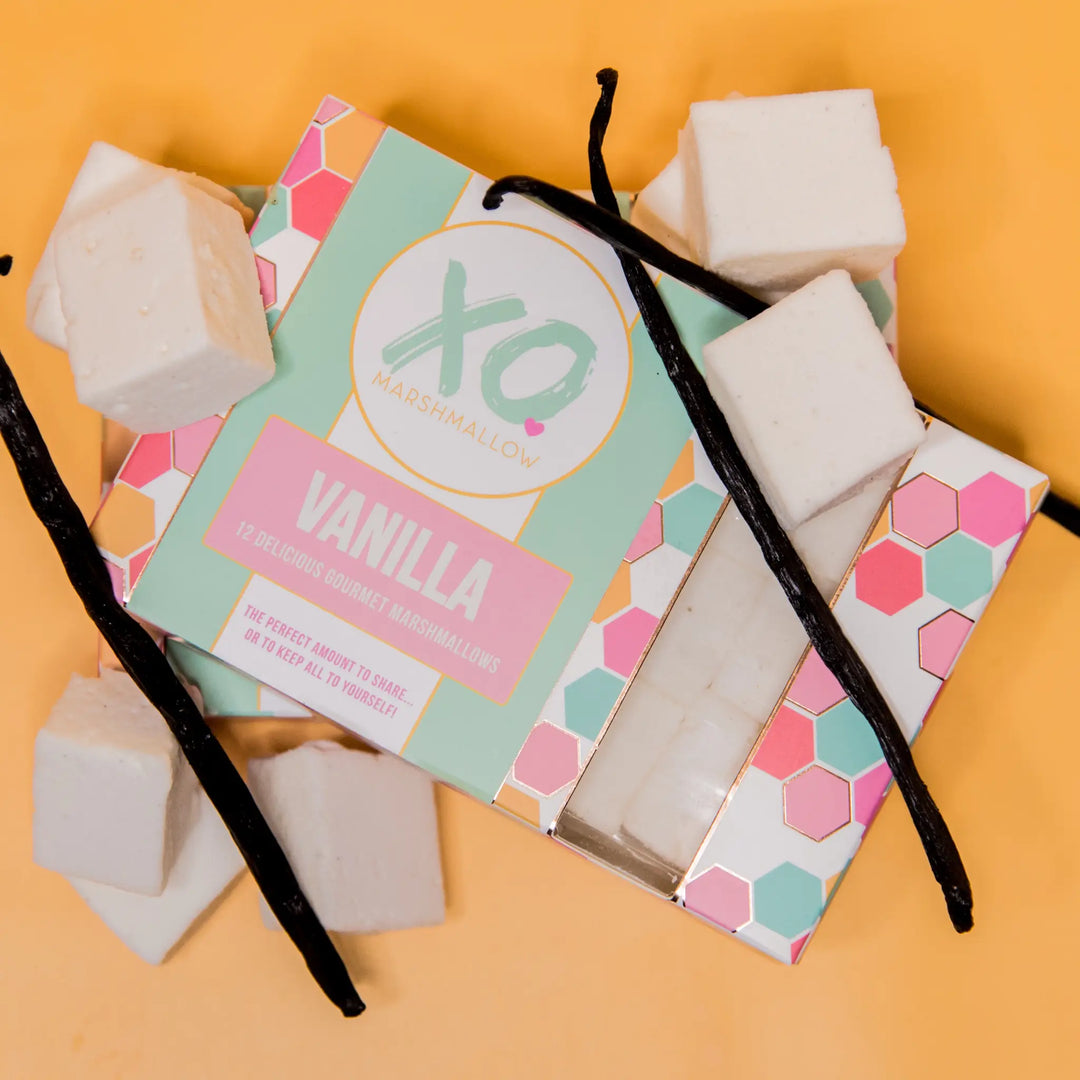 XO Vanilla marshmallow box surrounded by marshmallow cubes and vanilla bean pods on an orange background