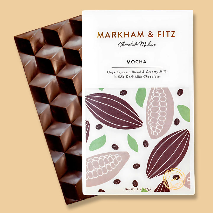 Cream and gold Markham &amp; Fitz Mocha bar sleeve lying across a glossy brown chocolate bar molded in raised cubes