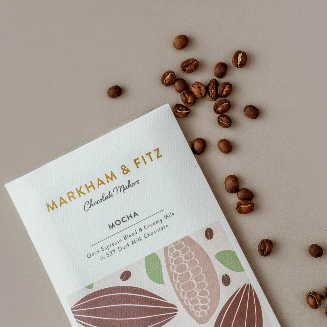 Mocha bar sleeve on a grey surface with roasted coffee beans scattered beside it