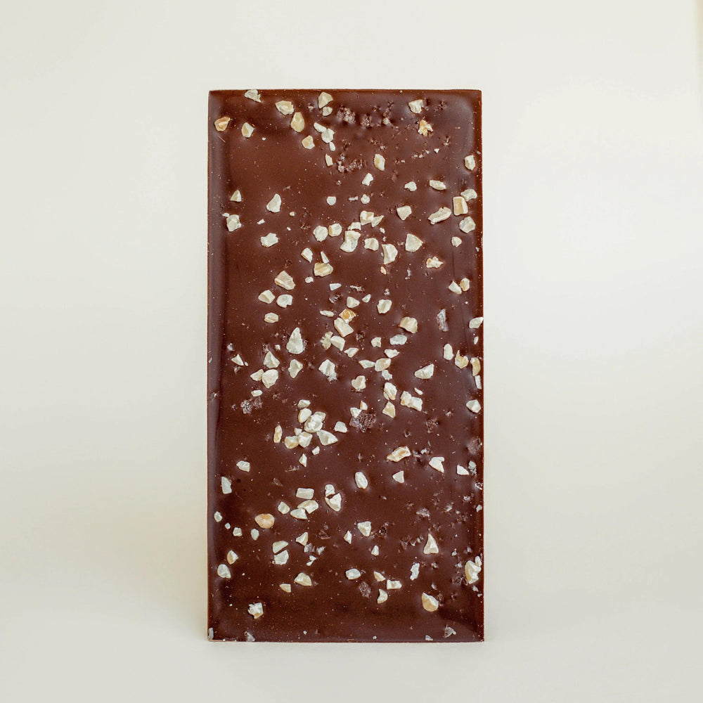 Unwrapped dark chocolate bar topped with chopped toasted almonds and coarse salt crystals