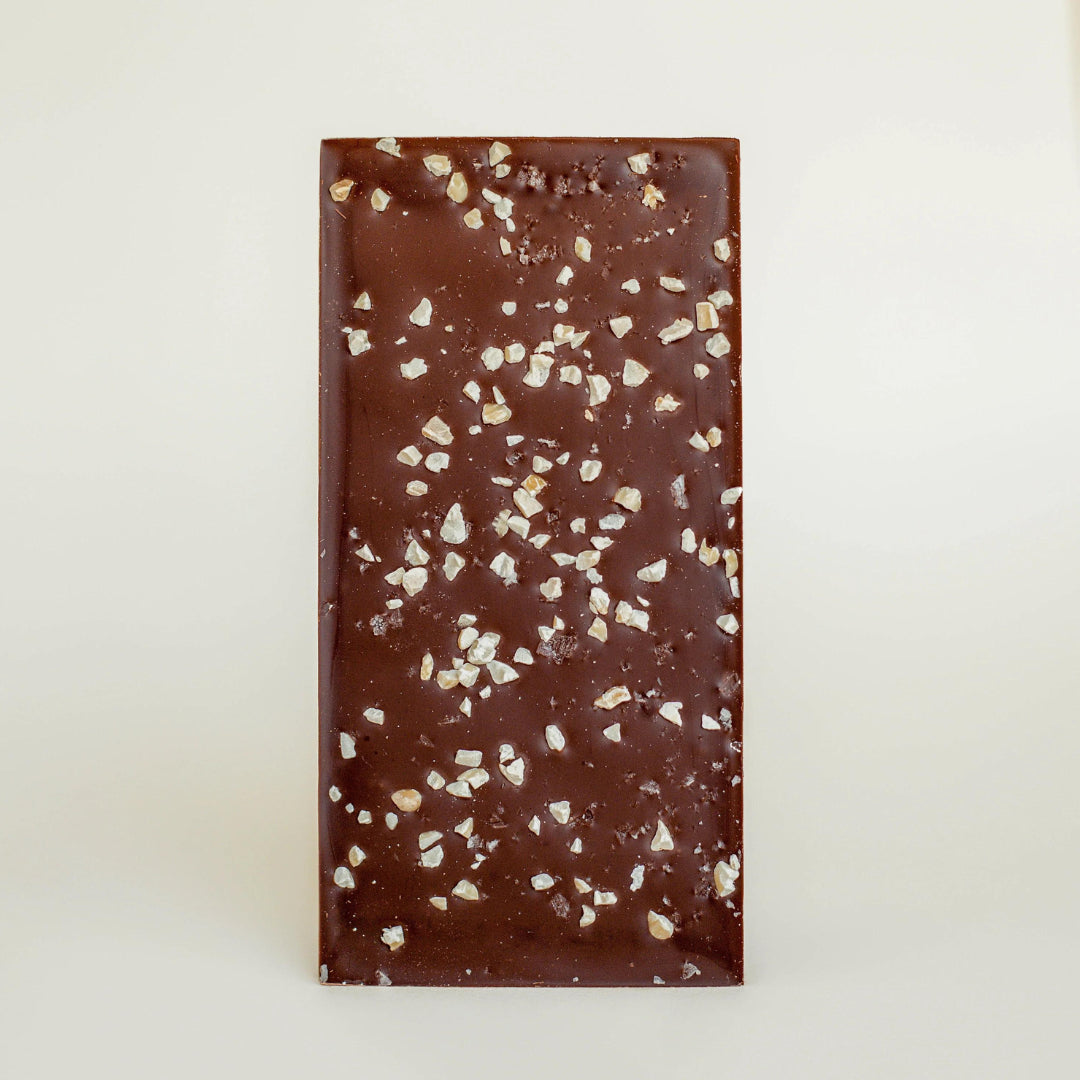 Unwrapped dark chocolate bar topped with chopped toasted almonds and coarse salt crystals