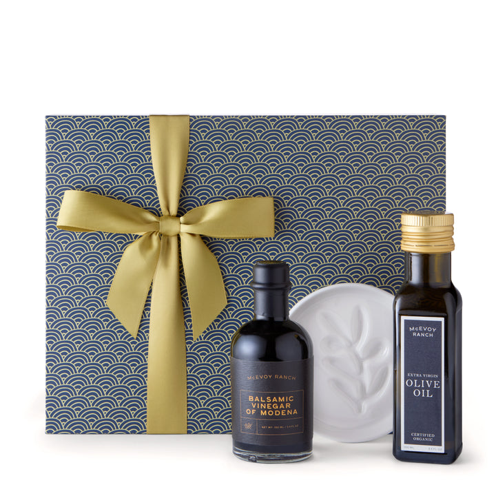 Navy and gold McEvoy Ranch gift box with a bottle of olive oil, a bottle of Modena balsamic vinegar and a white ceramic olive branch dipping dish