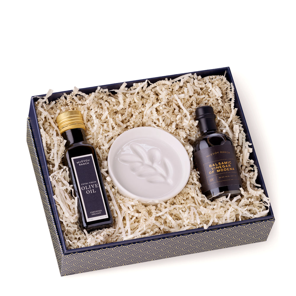 Open McEvoy Ranch gift box lined with cream crinkle paper holding the olive oil, balsamic vinegar and white ceramic dipping dish