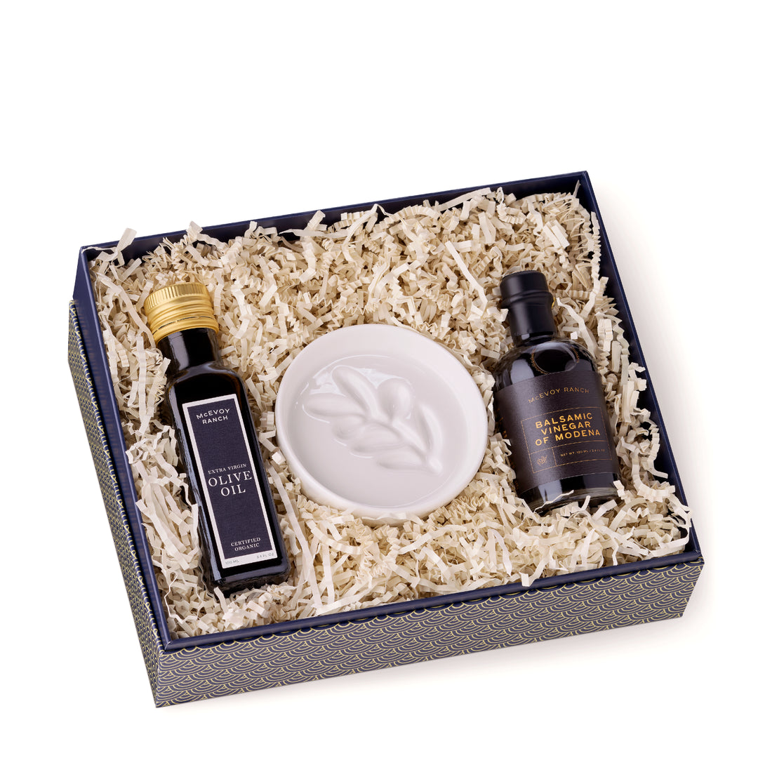 Open McEvoy Ranch gift box lined with cream crinkle paper holding the olive oil, balsamic vinegar and white ceramic dipping dish
