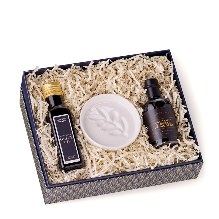 Open McEvoy Ranch gift box lined with cream crinkle paper holding the olive oil, balsamic vinegar and white ceramic dipping dish