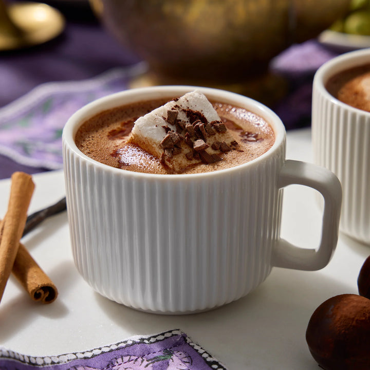 Ribbed white mug of dark drinking chocolate topped with a marshmallow and chocolate shavings