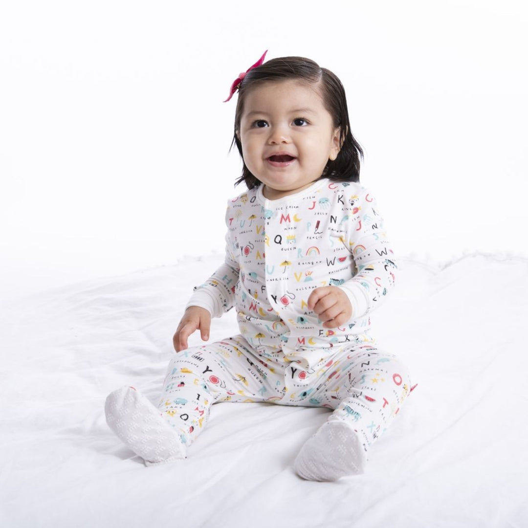 Baby wearing alphabet print footed pajamas sitting on a white blanket