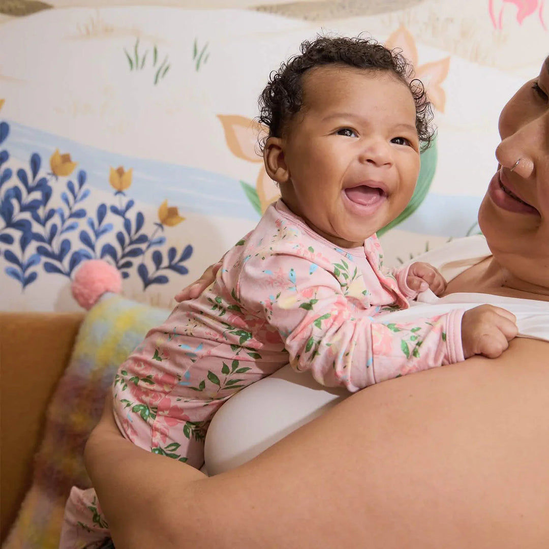 Smiling baby in pink floral footie pajamas held by adult in a nursery setting