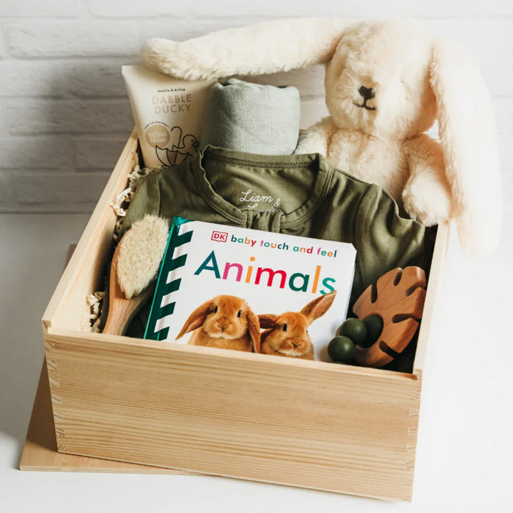 Baby gift box with onesie, book, and plush toy on a light background