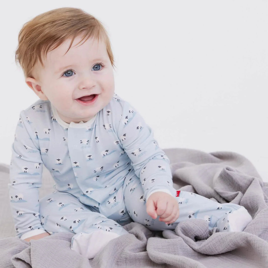 Baby in blue sheep-print footie pajamas sitting on a soft grey blanket