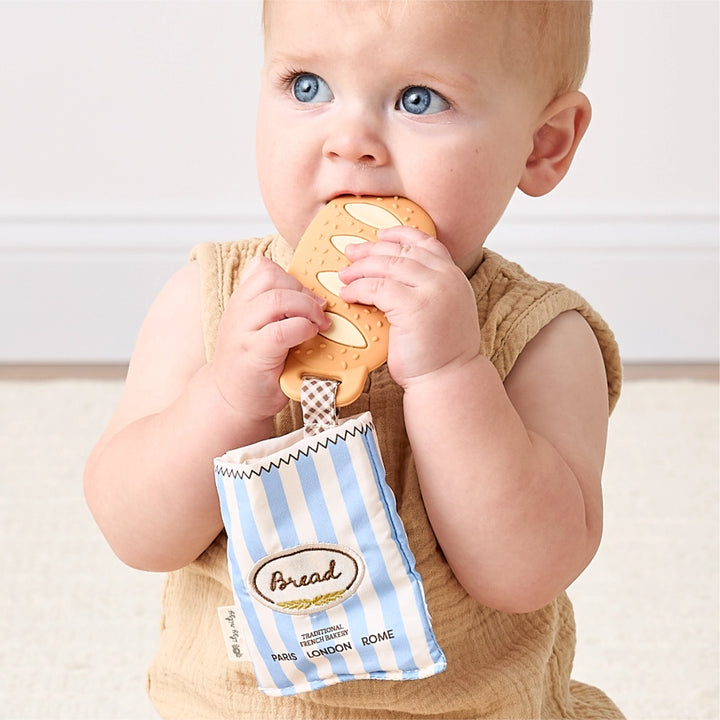 Baby holding a baguette-shaped teether toy with striped bread-themed pouch