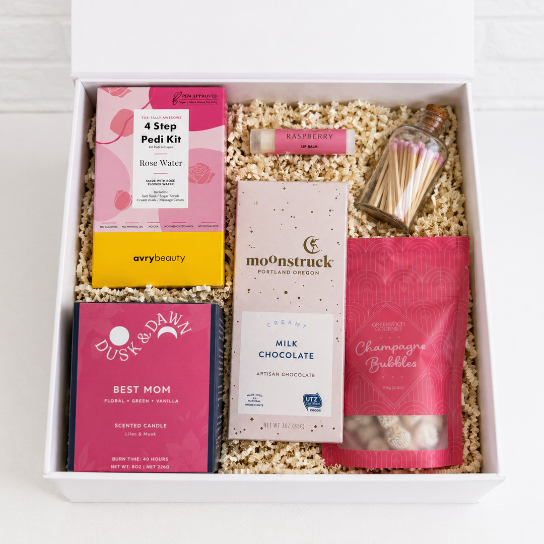 Gift box with various items including a pedicure kit, chocolate, and candles on a light background